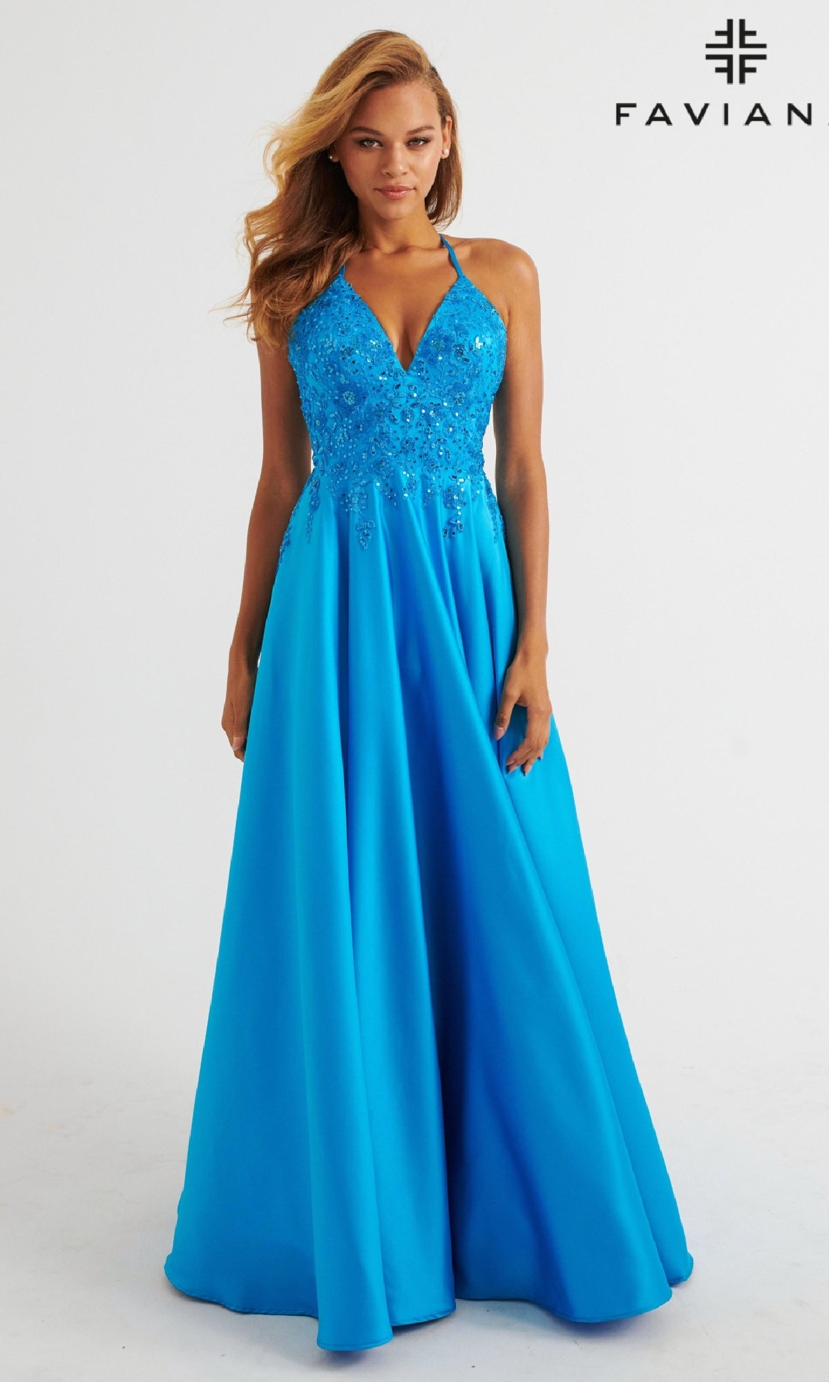 A woman wears the Faviana 11260 long prom dress—bright blue satin with floral embellishments, V-neckline, thin straps, and elegant lace-embroidered bodice.